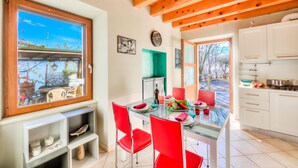A modern kitchen with white cabinets, a dining table with red chairs, and a large window overlooking a garden. - Faby House On Hilly Area And Lake View (Gargnano)