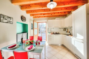 Un comedor con una mesa de vidrio, sillas rojas y una cocina con armarios blancos.