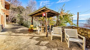 A covered outdoor seating area with a table and chairs, a stone wall, and a view of the sea. - Faby House On Hilly Area And Lake View (Gargnano)