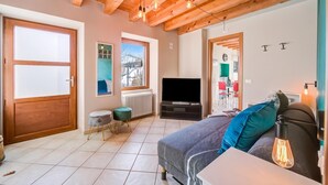 A cozy room with a wooden ceiling, a television, a sofa with cushions, a small table, and a window with a view. - Faby House On Hilly Area And Lake View (Gargnano)