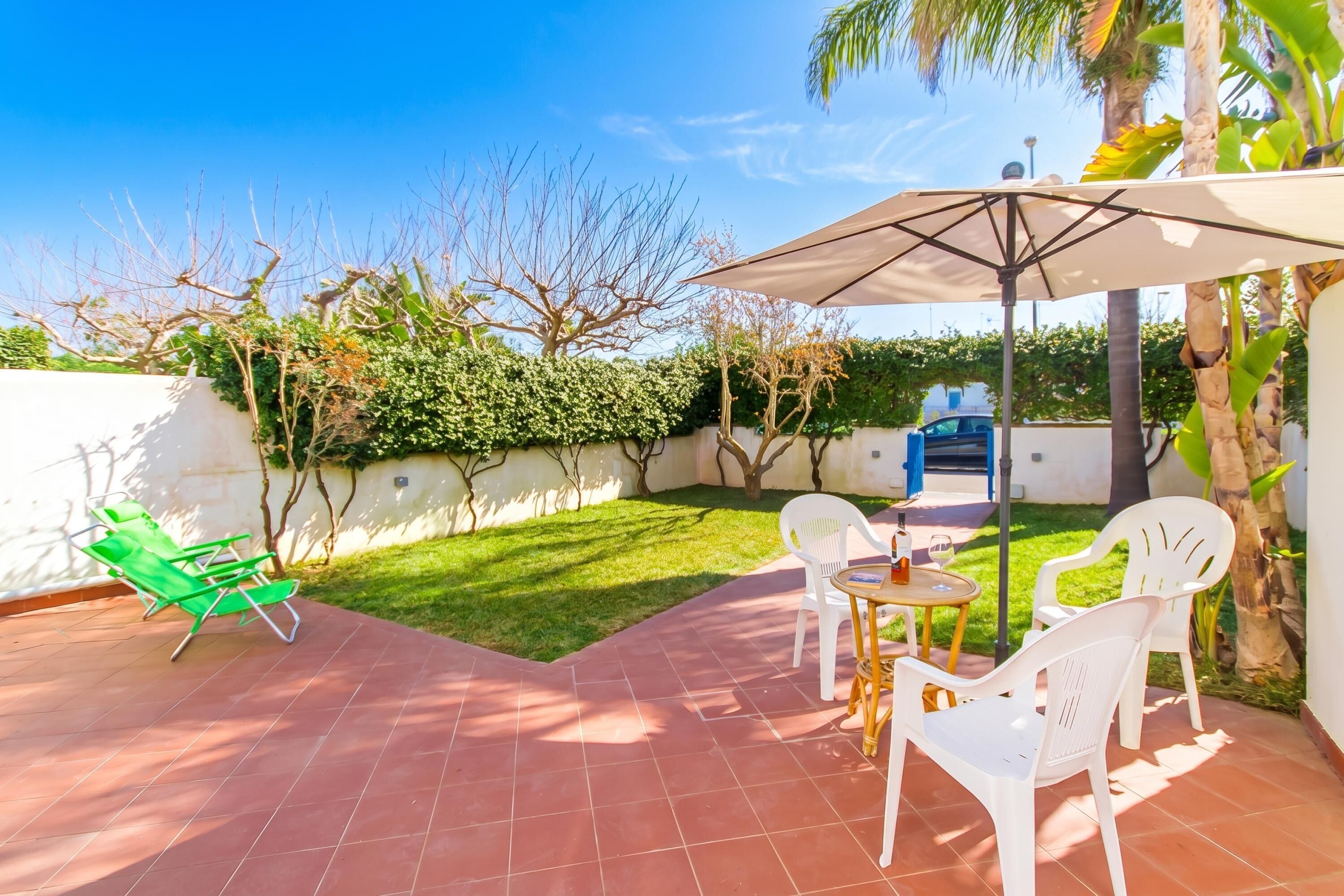 Un patio con mesa y sillas, una silla lounge verde y una sombrilla.