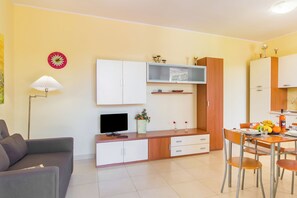 A compact living space with a sofa, a dining table with chairs, a TV, a cabinet, and a small plant. - Villetta Relax with pool in residence (Melendugno)