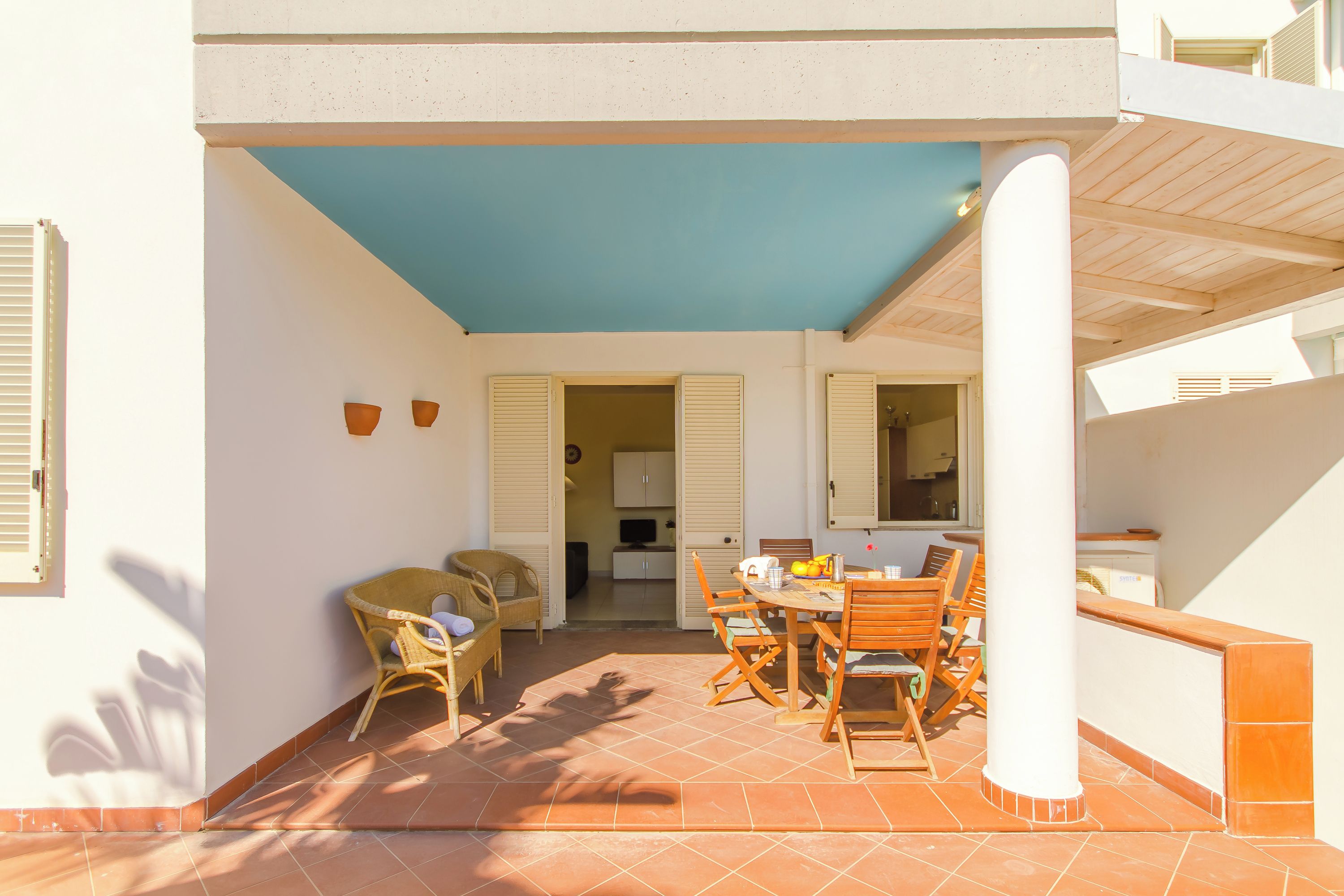 Un patio al aire libre con una mesa, sillas y una silla de mimbre, con vistas a la casa.