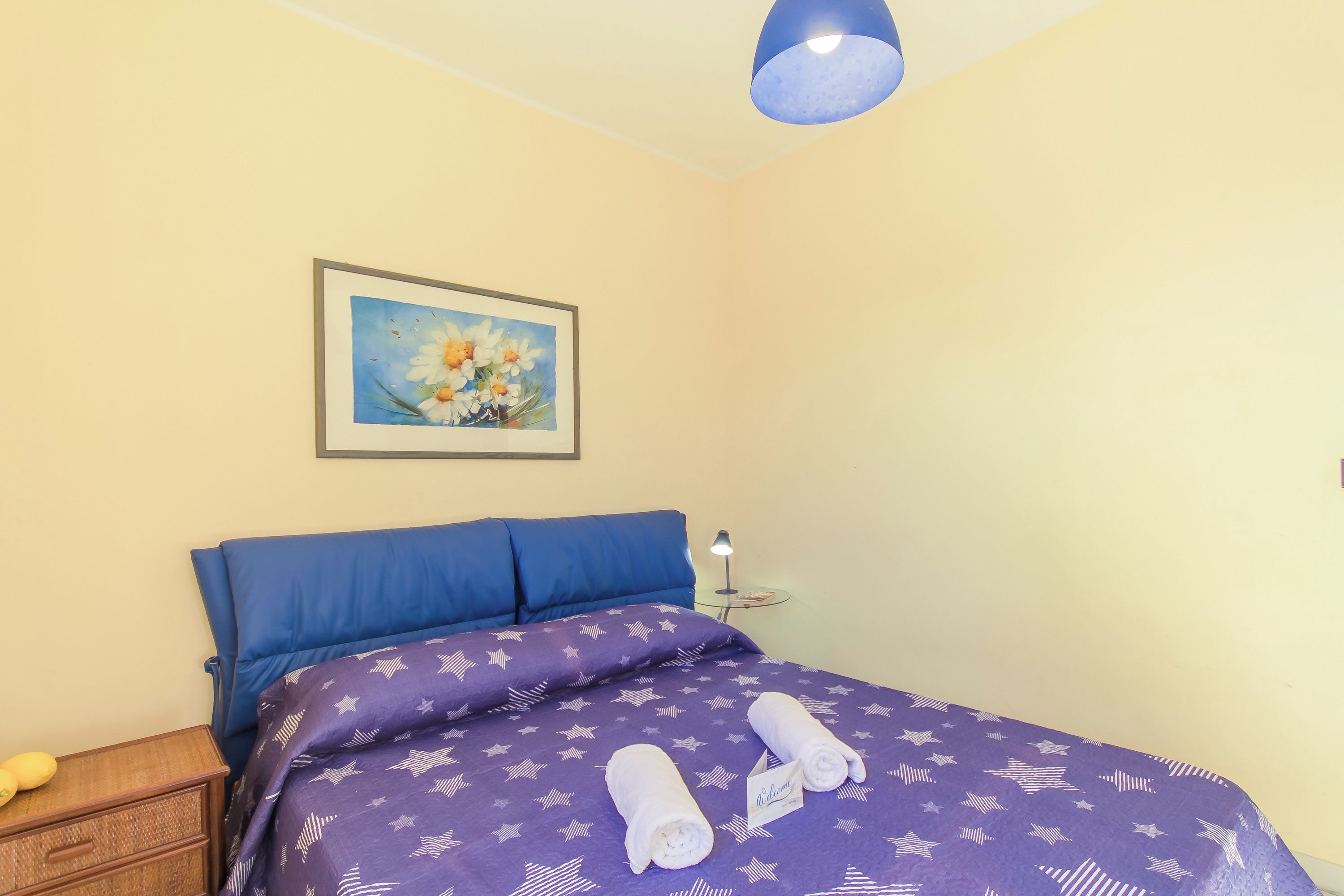 A hotel room with a bed, a nightstand, a lamp, and a painting on the wall.