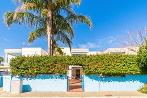 A modern building with a blue wall and a palm tree. - Villetta Relax with pool in residence (Melendugno)