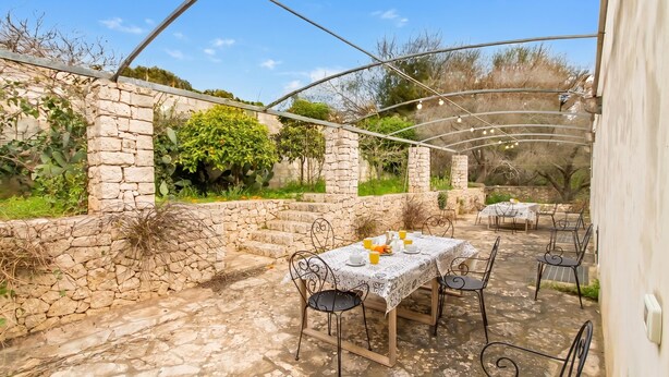 Eine Terrasse im Freien mit Steinmauern, einem überdachten Sitzbereich und einem Tisch für zwei Personen.