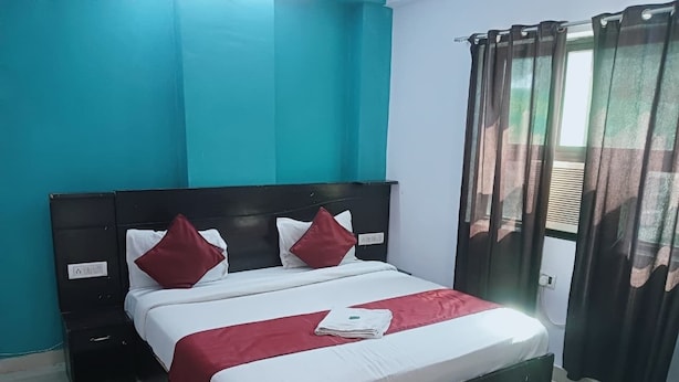 A neatly made bed with white and red bedding, a black headboard, and two pillows. - Hotel Quality Time  (Udaipur)
