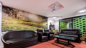 A living room with a large mural, leather sofas, a glass coffee table, and a bookshelf. - Hotel Quality Time  (Udaipur)