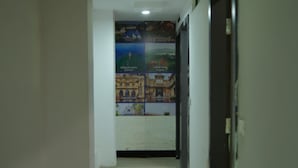 A hallway with a poster on the wall, a door on the right, and a tiled floor. - Hotel Quality Time  (Udaipur)