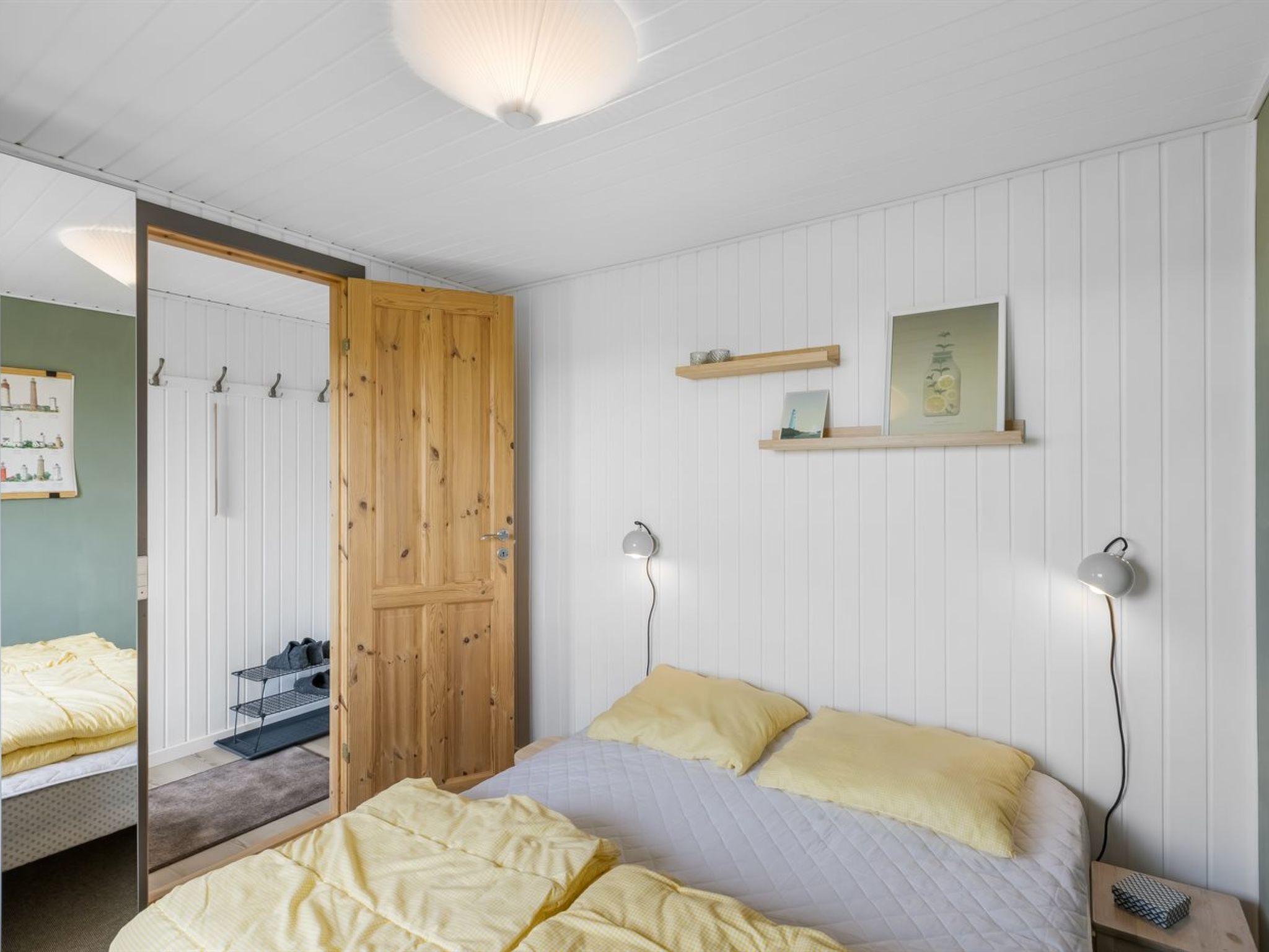 A bedroom with a bed, bedside lamps, a wooden wardrobe, and a mirror.