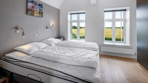 Een slaapkamer met een groot bed, twee bedlampjes, een schilderij aan de muur en uitzicht op een veld door een raam.
