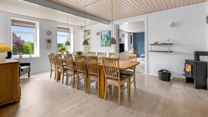Een ruime eetruimte met een houten tafel en stoelen, grote ramen en een modern plafondontwerp.