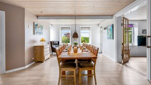 Een ruime eethoek met een lange houten tafel, comfortabele stoelen en een hanglamp.