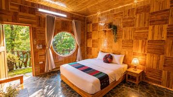 Una habitación con paneles de madera, una cama, un ventanal redondo y suelo de piedra.