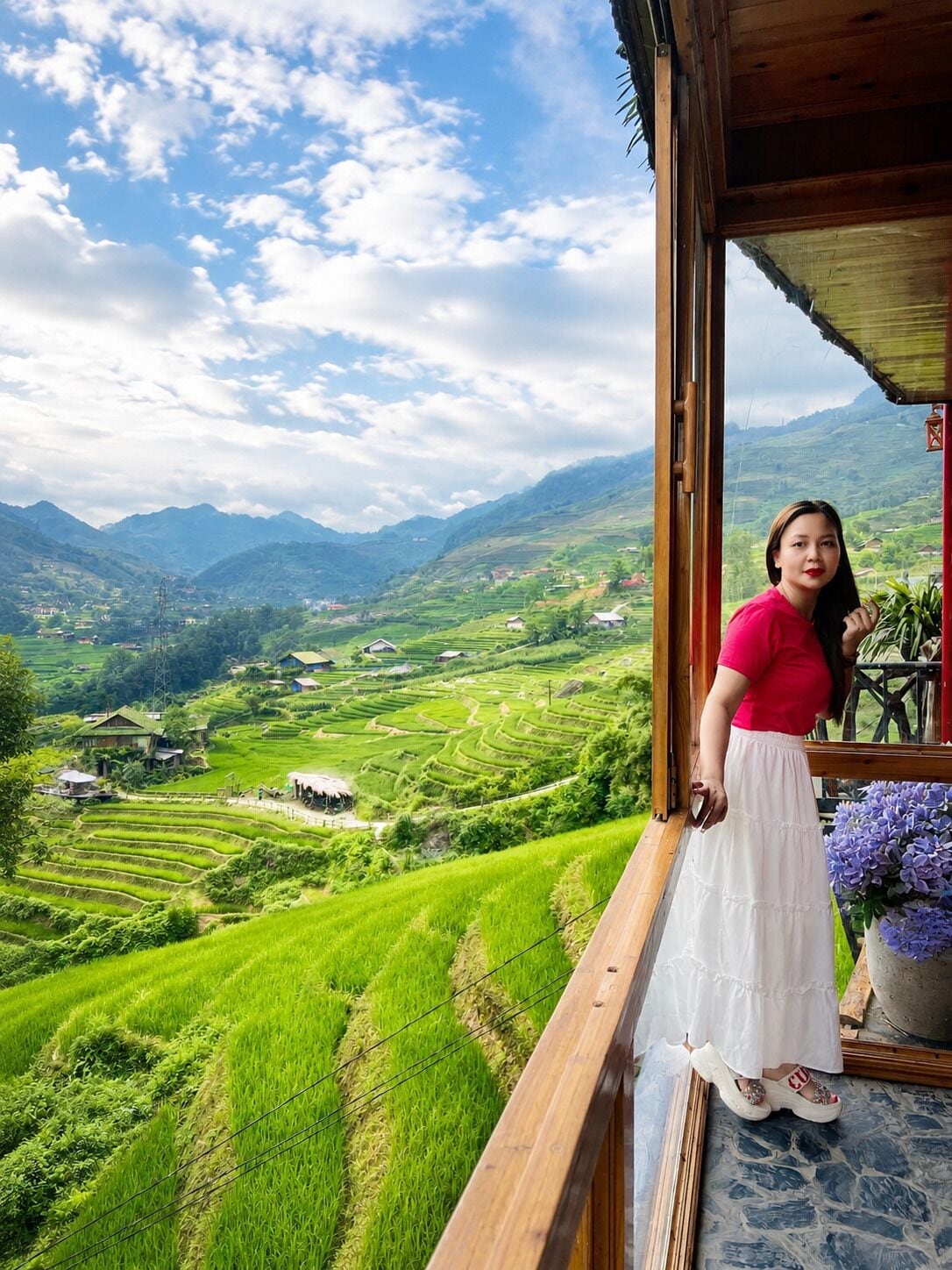 A person standing on a balcony with a view of terraced fields and mountains.