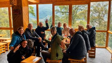 Un grupo de personas sentadas alrededor de una mesa dentro de una cabaña de madera con ventanas amplias que dan a una vista del exterior.