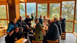A group of people seated around a table inside a wooden cabin with large windows offering a view of the outdoors. - MT House Sa Pa (Sa Pa)