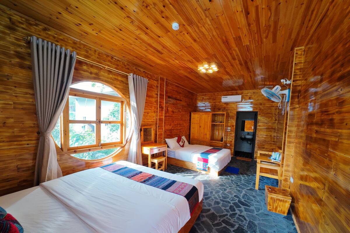 Ein Zimmer in einer Holzhütte mit zwei Betten, einem kleinen Tisch, einem Spiegel und einem Fenster mit Vorhängen.