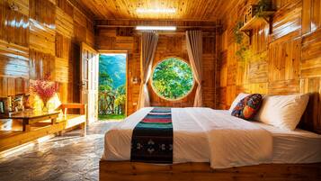 Habitación de cabaña de madera con cama, una mesa con aperitivos, un ventilador y ventana con vista a follaje.