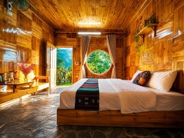 Habitación de cabaña de madera con cama, una mesa con aperitivos, un ventilador y ventana con vista a follaje.