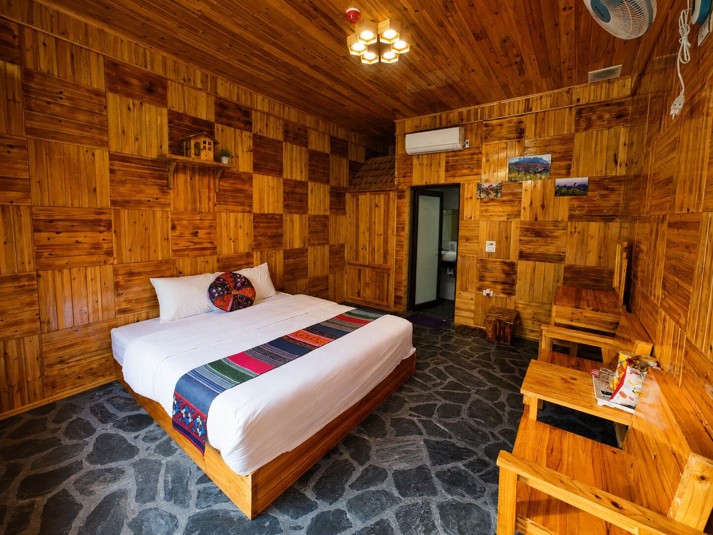 Una habitación de madera con una cama, una mesita pequeña y suelo de piedra.