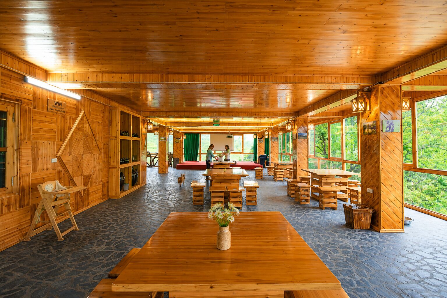 A wooden interior with a central table, benches, and a stage area.