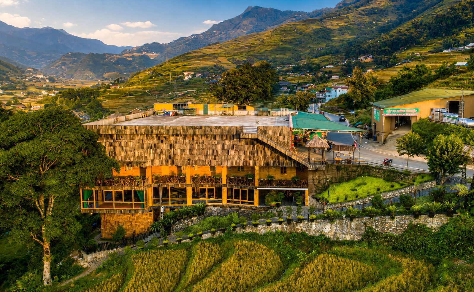 A wooden building with a terrace, surrounded by terraced fields and mountains.