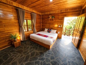 A wooden cabin bedroom with a stone floor, a bed with a red and blue blanket, and a window with curtains. - MT House Sa Pa (Sa Pa)