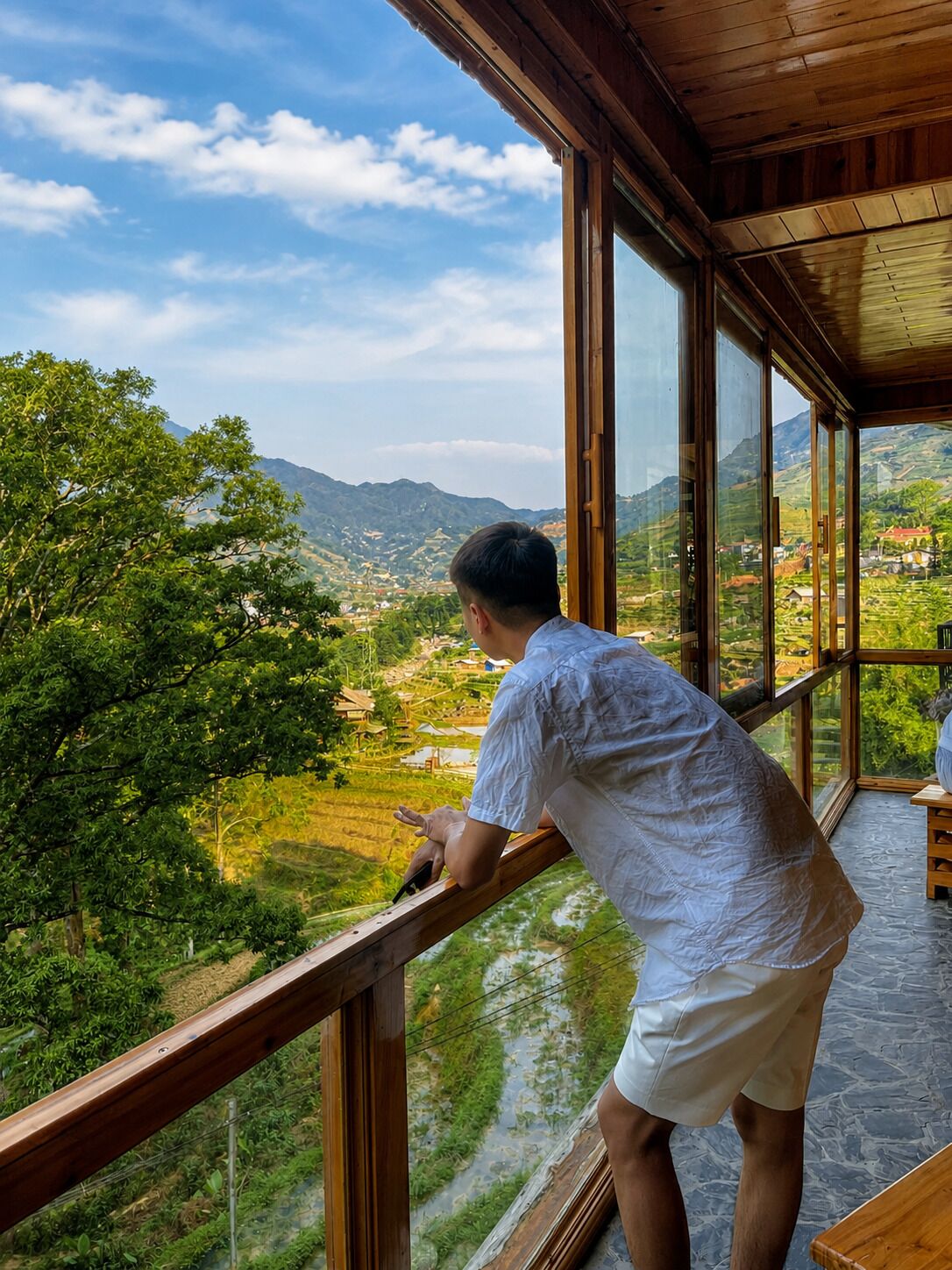 Une personne appuyée sur la balustrade d’un balcon, d’où l’on peut admirer un paysage magnifique avec des montagnes et une rivière.