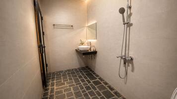Un baño moderno con piso de baldosas de piedra, ducha con rociador circular y lavamanos con espejo.