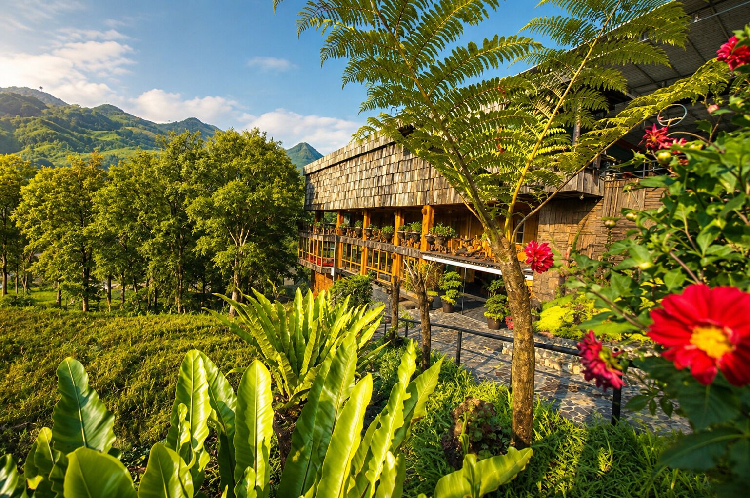 A building with a wooden facade and a balcony overlooking a lush garden with various plants and flowers.