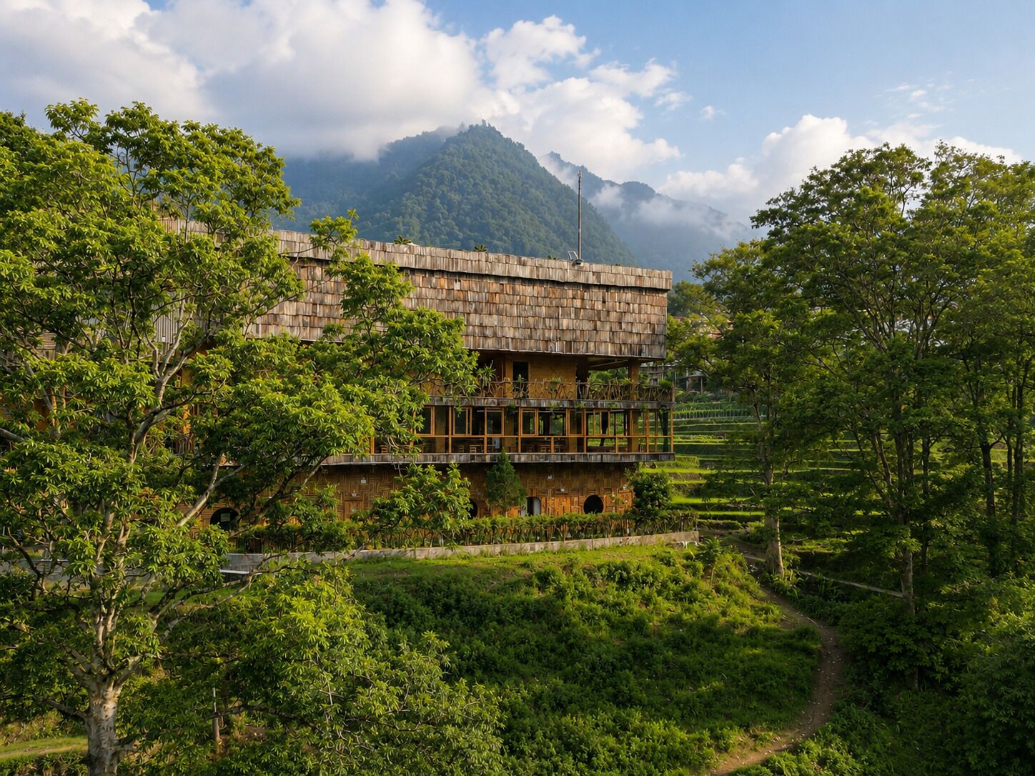 Un edificio de varios pisos con un estilo arquitectónico tradicional, rodeado de exuberante vegetación y un telón de fondo montañoso.