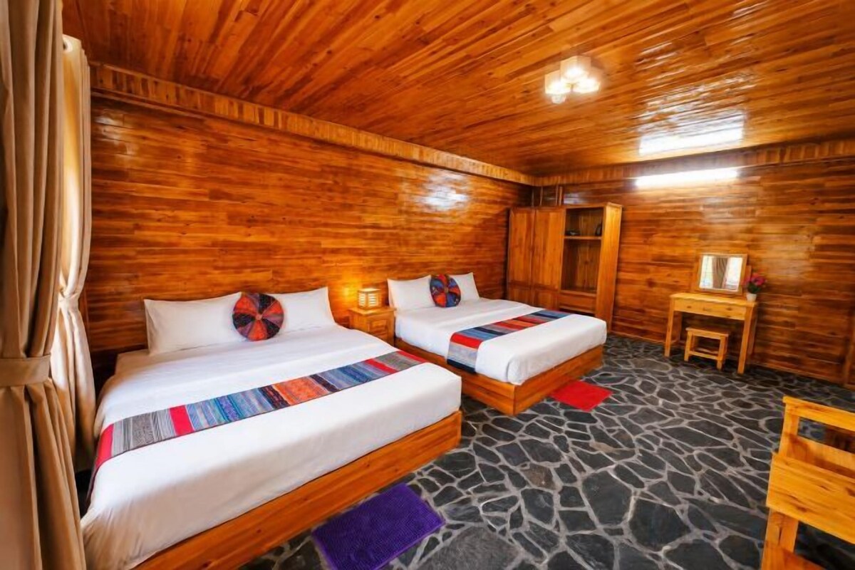 A wooden cabin room with two beds, a small table, and a stone floor.