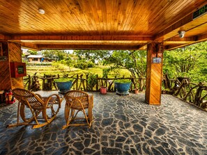 A covered outdoor seating area with stone flooring and wooden furniture, overlooking a lush green landscape. - MT House Sa Pa (Sa Pa)