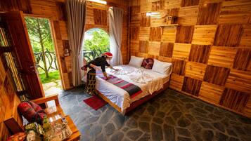 A wooden cabin room with a bed, a table with items, and a view of greenery outside.