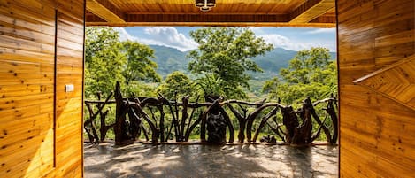 A wooden interior with a stone floor leading to an outdoor area with a view of green trees and mountains.