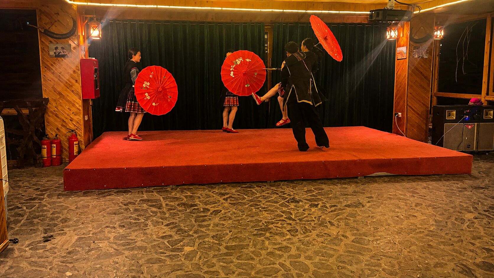 A stage with a red carpet and stone flooring, equipped with stage lights and sound equipment.