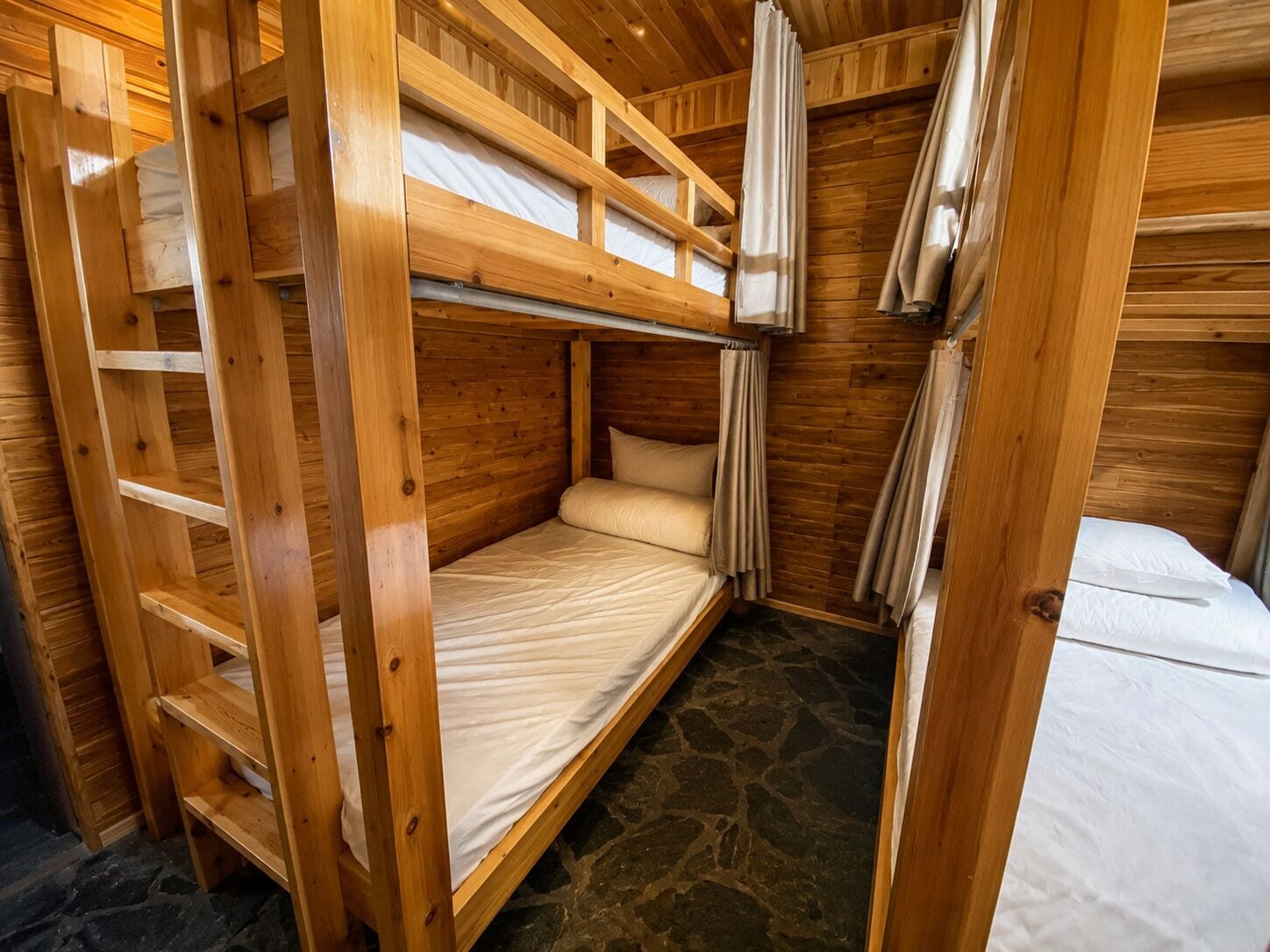 A wooden bunk bed room with a stone floor, a ladder, and curtains.