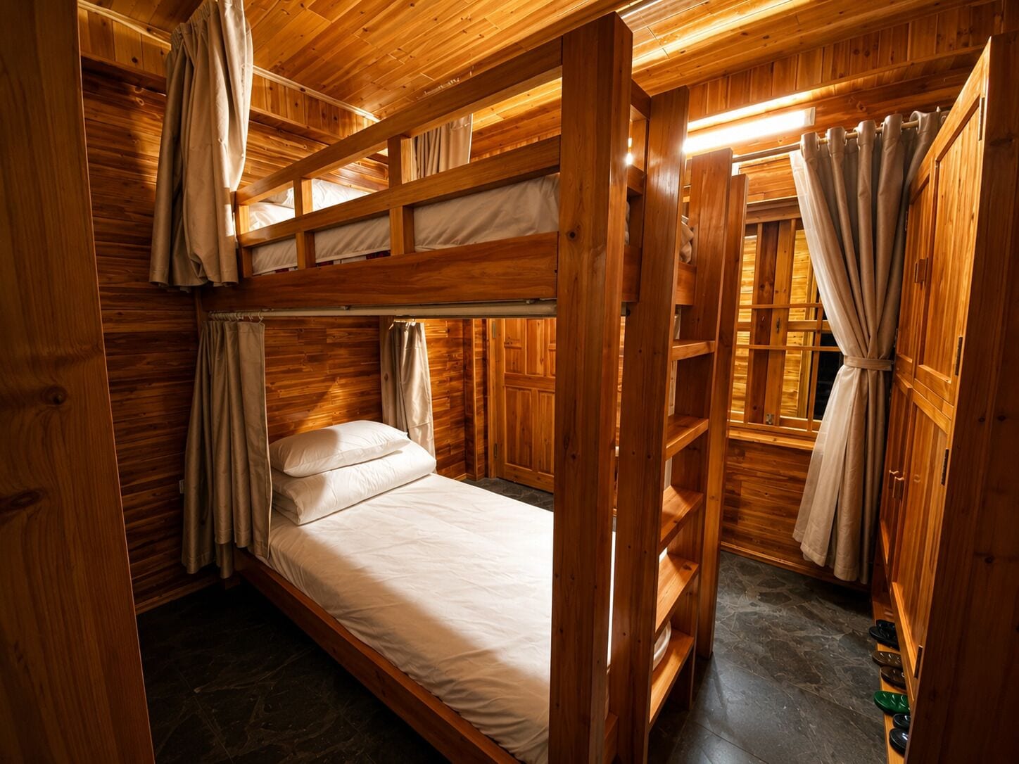 A wooden bunk bed room with a window and curtains.