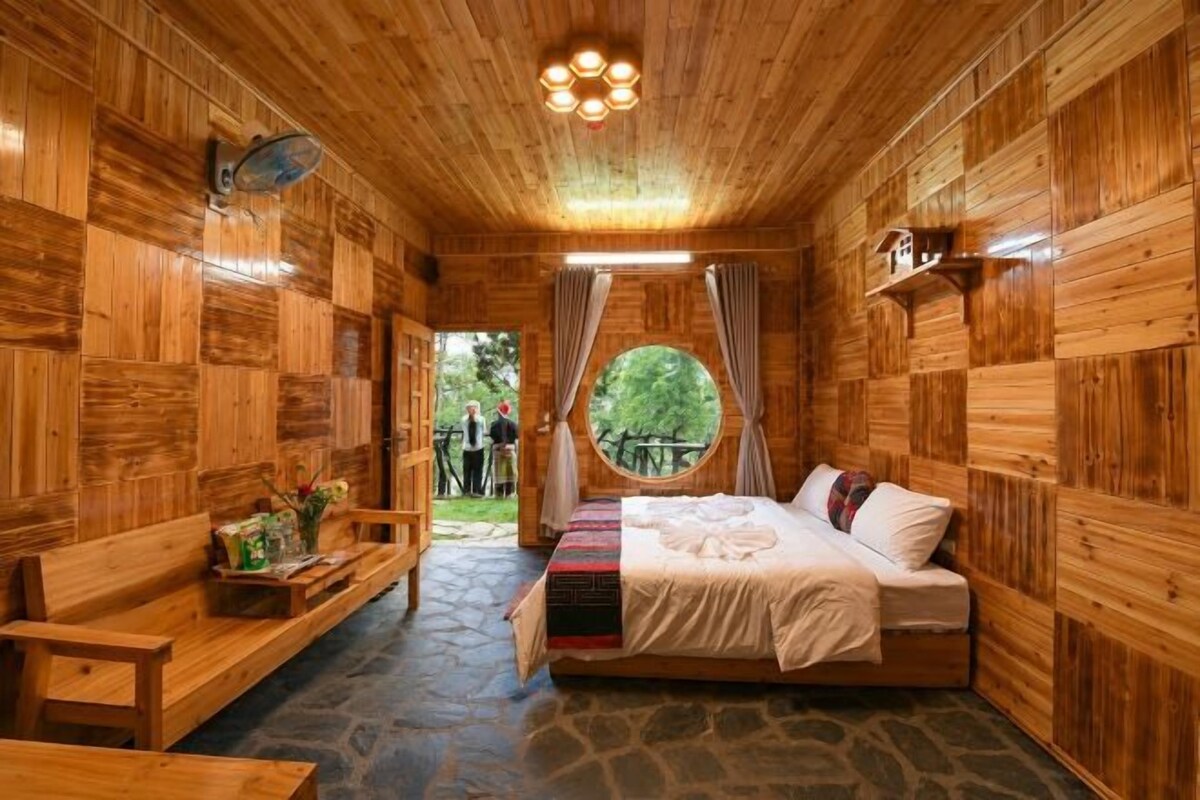 A wooden cabin room with a bed, a bench, and a window.
