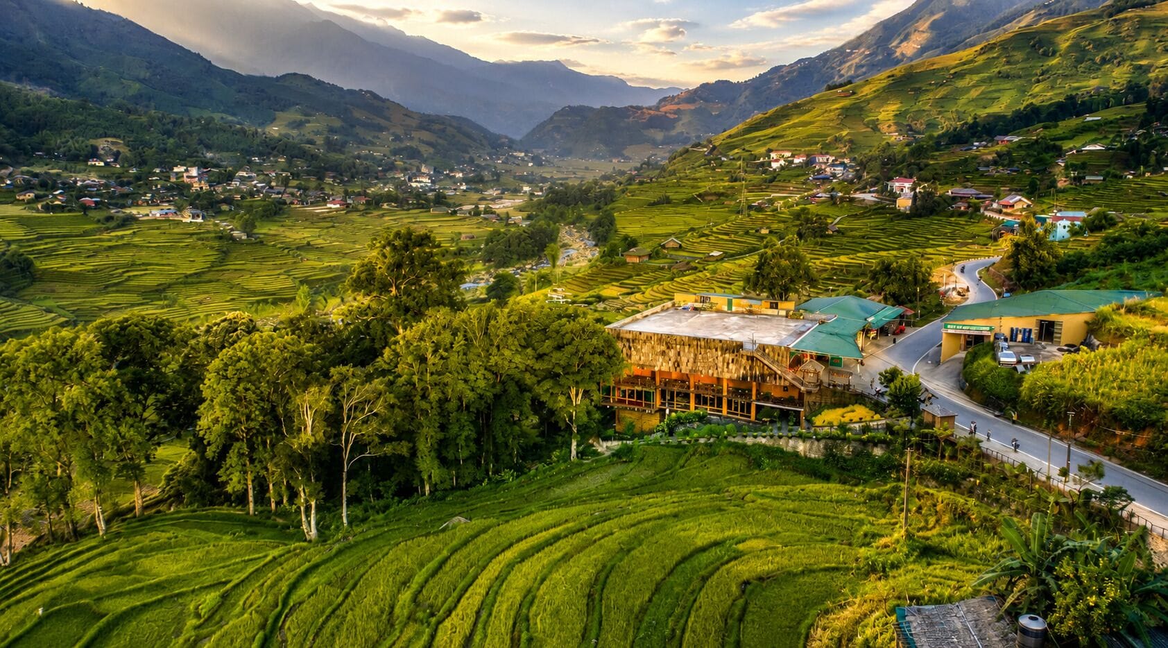 A rural landscape with terraced fields, a road, and a building with a green roof.