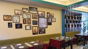 Un ristorante con tavoli apparecchiati per consumare il pasto, una parete decorata con quadri incorniciati e una panca imbottita verde lungo il muro.