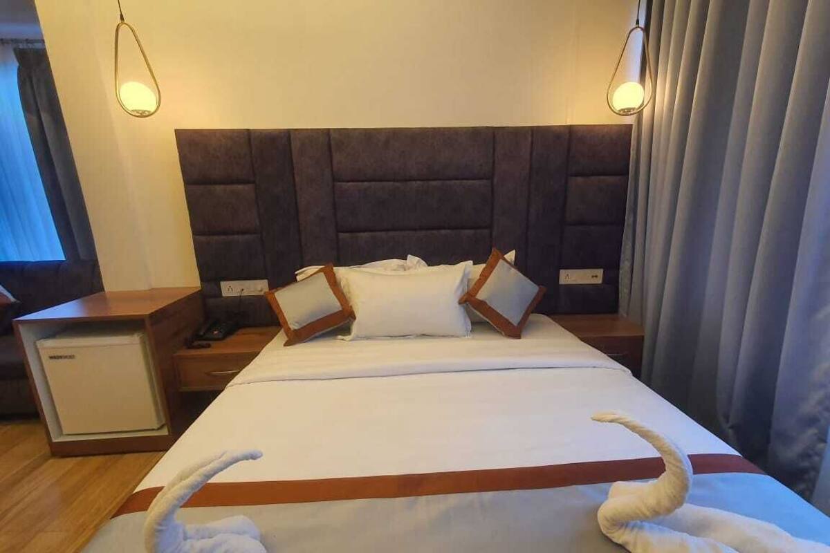 A hotel room with a large bed, a bedside table, a lamp, and a window with curtains.