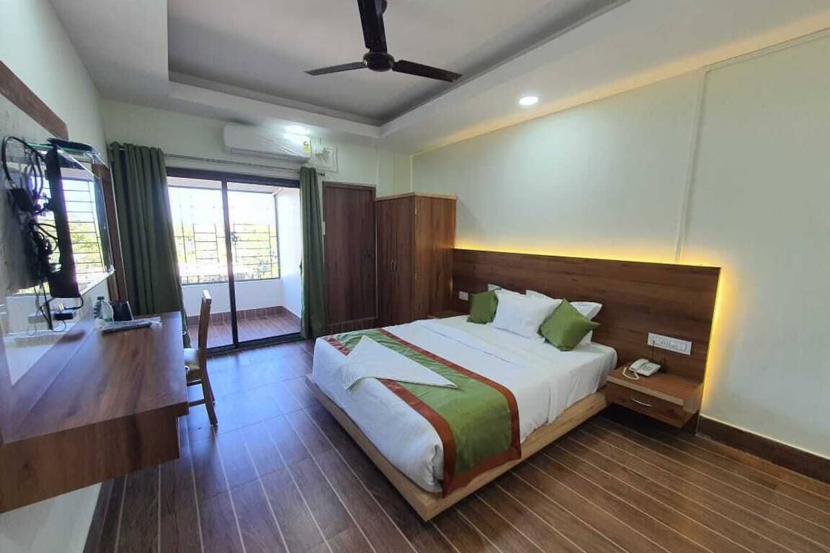 A hotel room with a bed, wooden headboard, bedside table, and a desk with a chair.