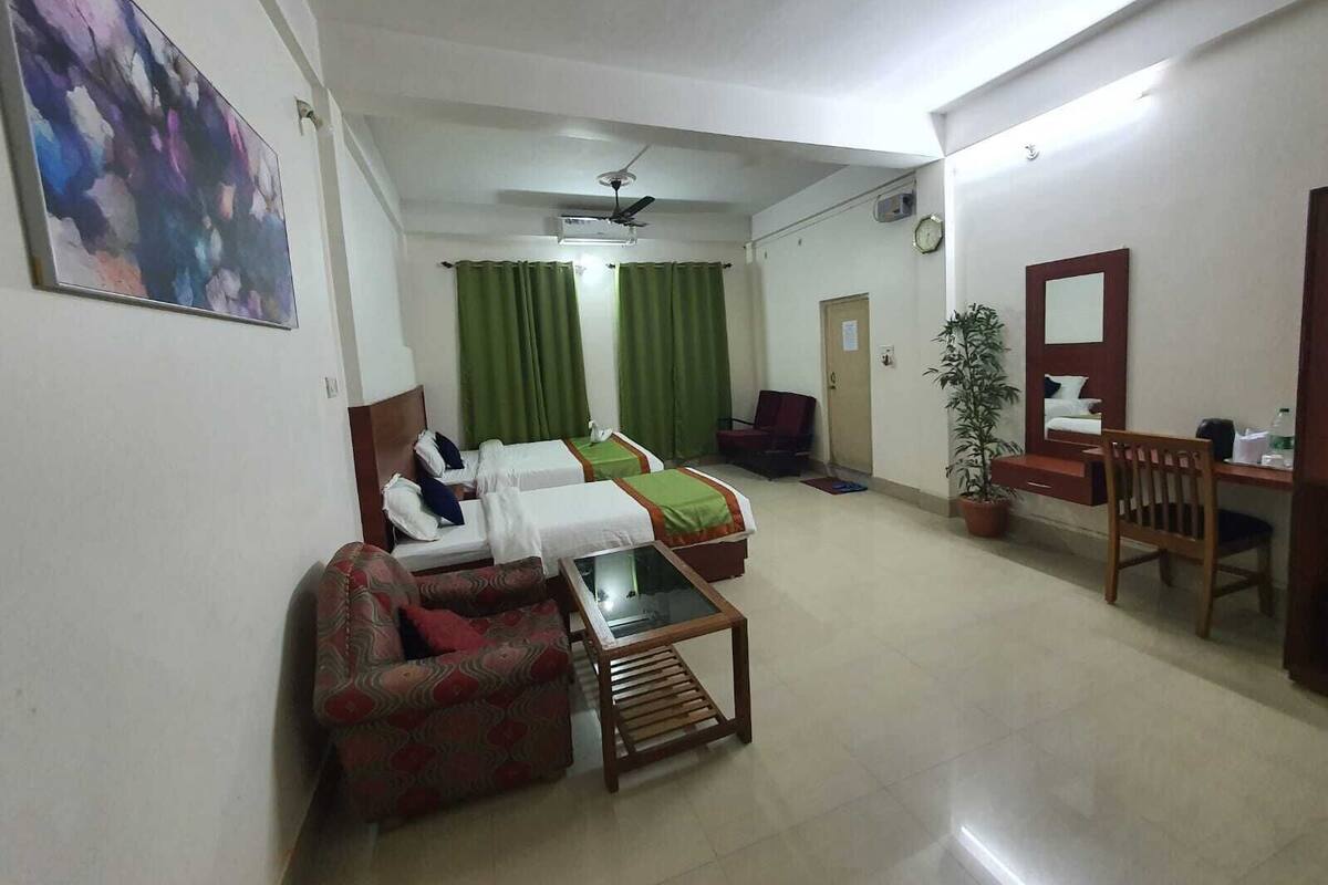 A hotel room with two beds, a sofa, a desk, a chair, a potted plant, and a ceiling fan.