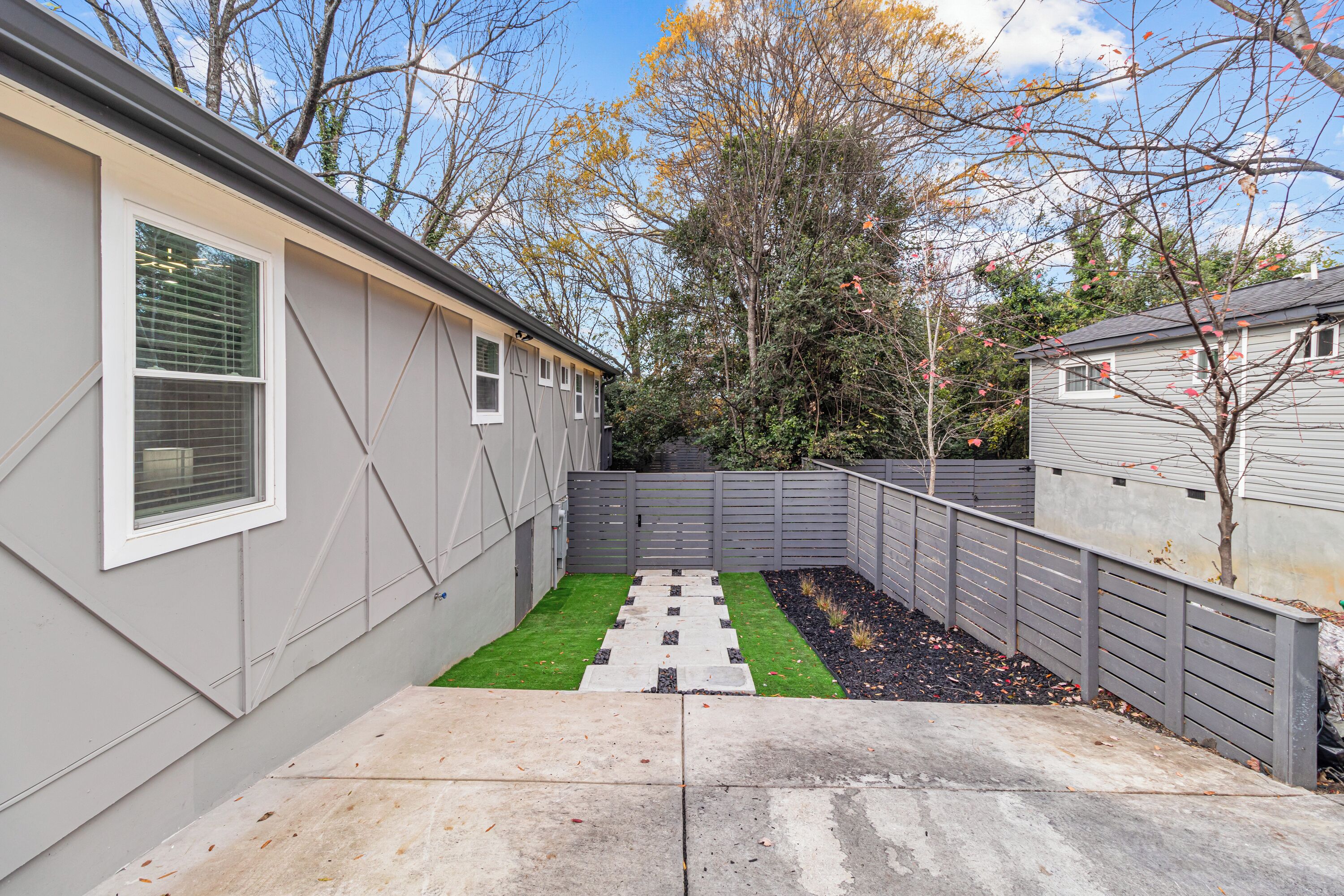 A residential backyard with a paved patio, a small lawn, and a wooden fence.