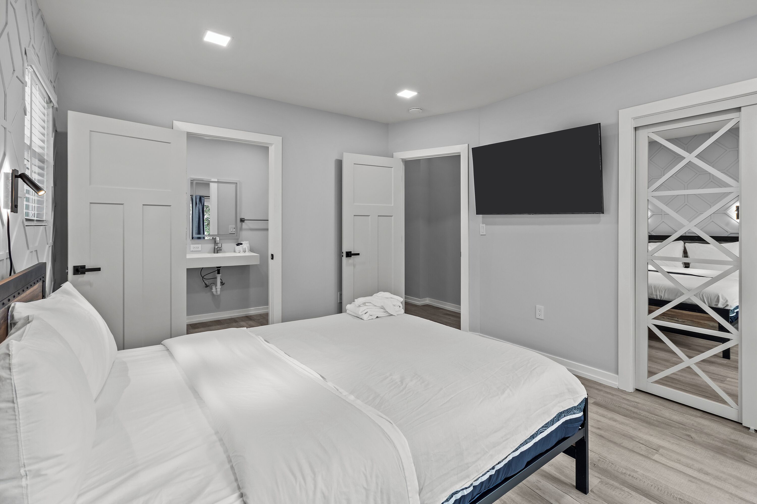 A bedroom with a large bed, a TV mounted on the wall, and a walk-in closet with a mirrored wardrobe.