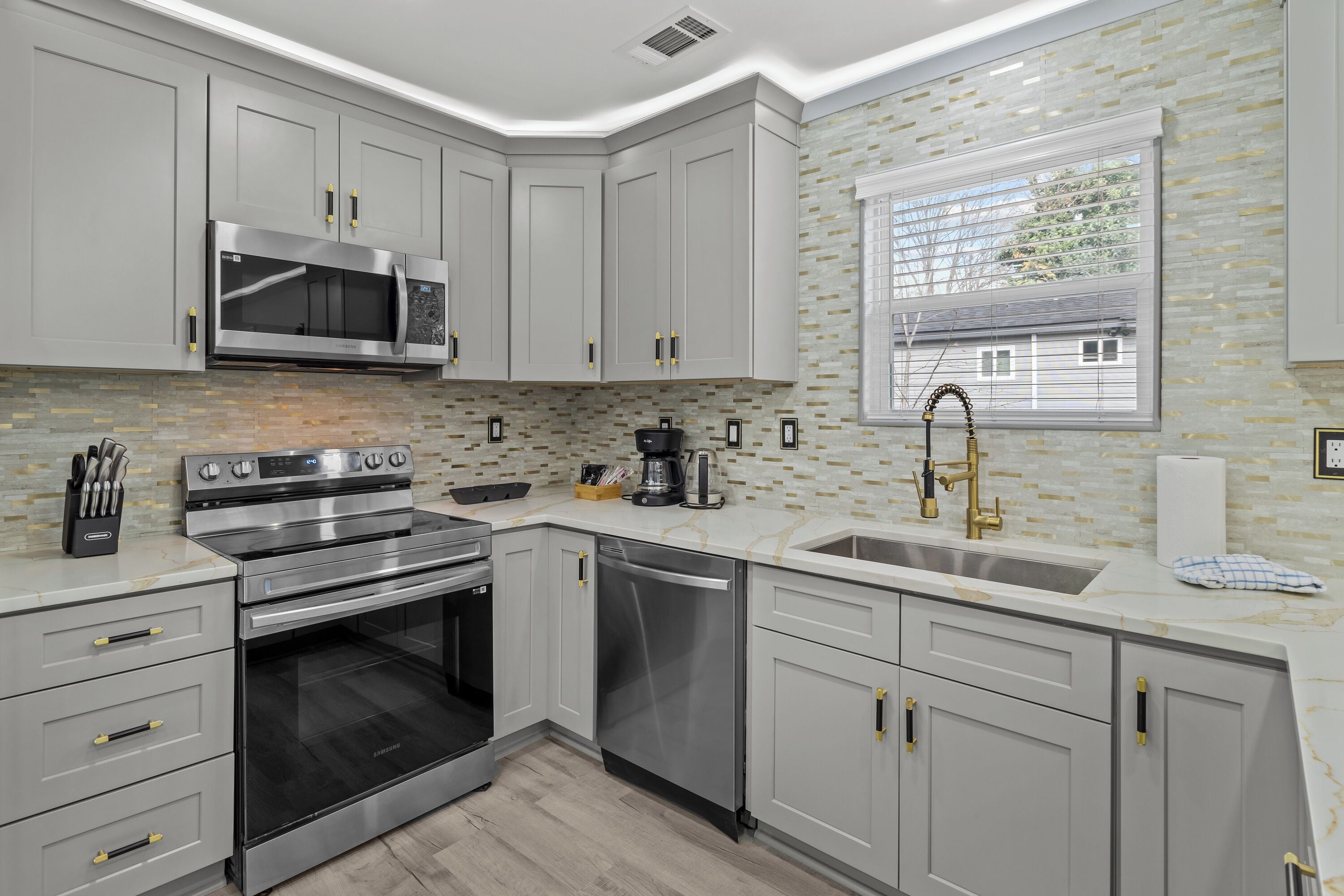 A modern kitchen with grey cabinets, stainless steel appliances, and a large window.