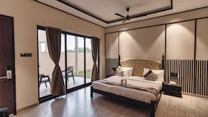A modern bedroom with a large bed, sliding glass doors leading to a balcony, and a ceiling fan. - The premier gir resort (Talala)