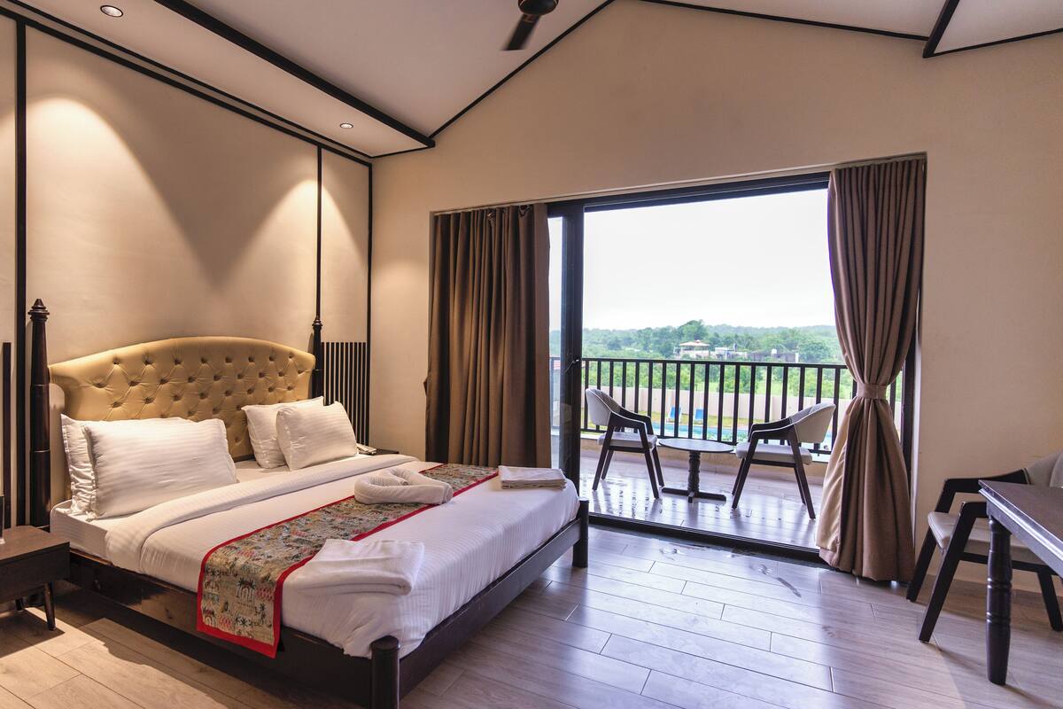 A bedroom with a large bed, a desk, and a balcony with chairs.